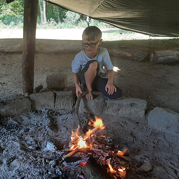 Eine Kind stochert mit einem Stock im Feuer.