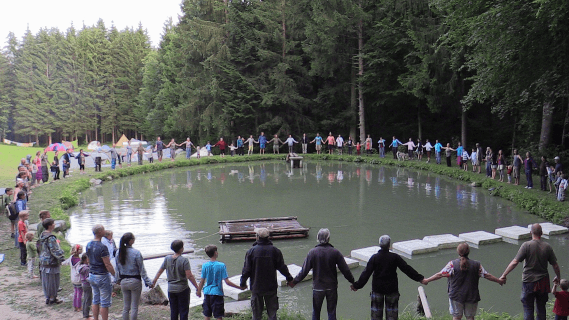 Über 100 Menschen stehen im Kreis um einen Teich und reichen sich die Hände.